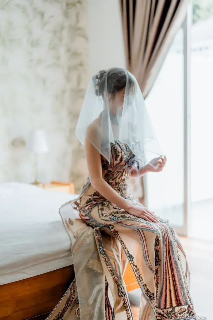 Bride sitting at the edge of a bed in a hotel room, wearing an ornate wedding dress —captured by Struck By Luna in Penang, Malaysia.